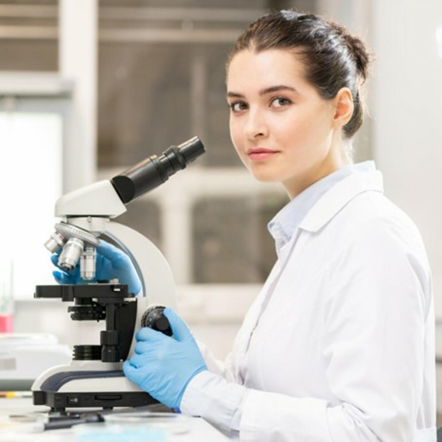 Une chercheuse en blouse blanche dans un laboratoire, manipulant un microscope