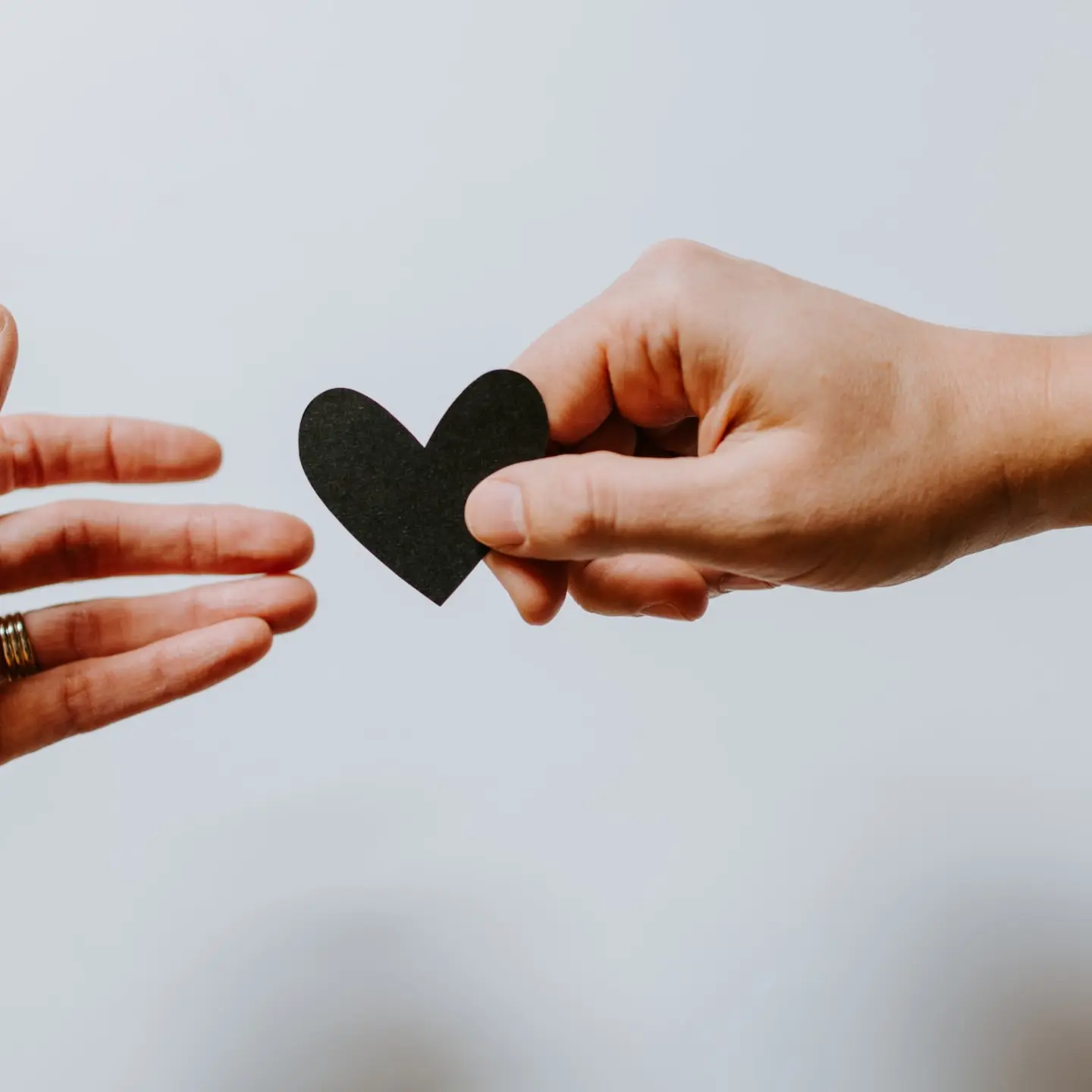 Faire un don IFI Deux mains qui se passe un coeur en papier noir
